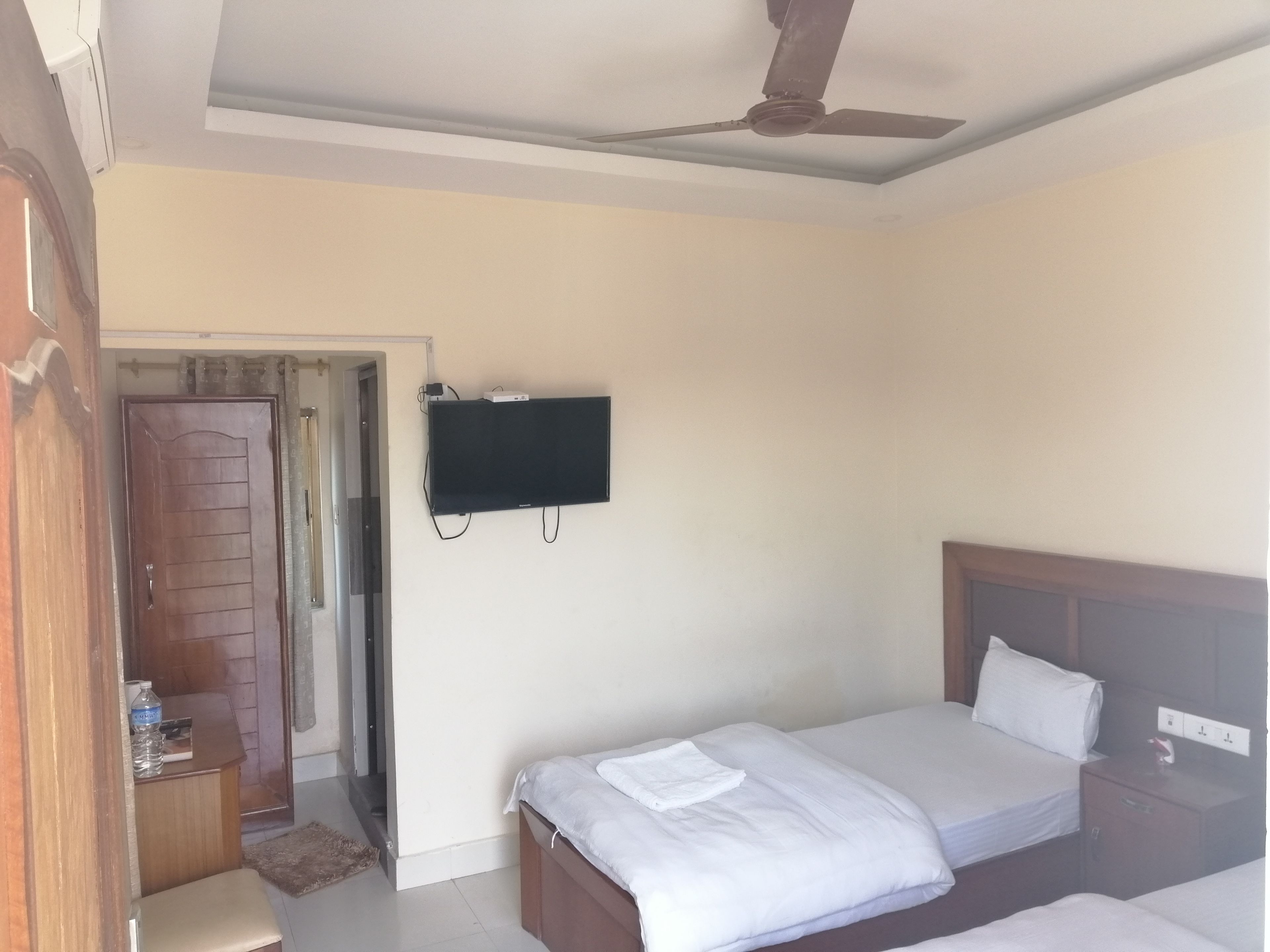 A hotel room with two beds, a ceiling fan, a TV mounted on the wall, and a wooden door.