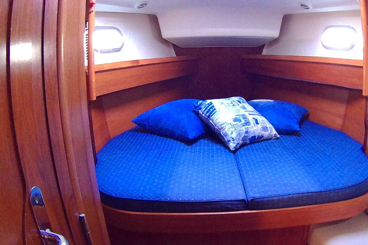 Un lit compact et incurvé, avec une literie bleue et des oreillers, dans une cabine aux boiseries et au chevet blanc.
