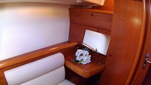 Een klein vakantiehuisje met een houten opbergmeubel, een witte zitting met kussen en een tafeltje met een bloemstuk.