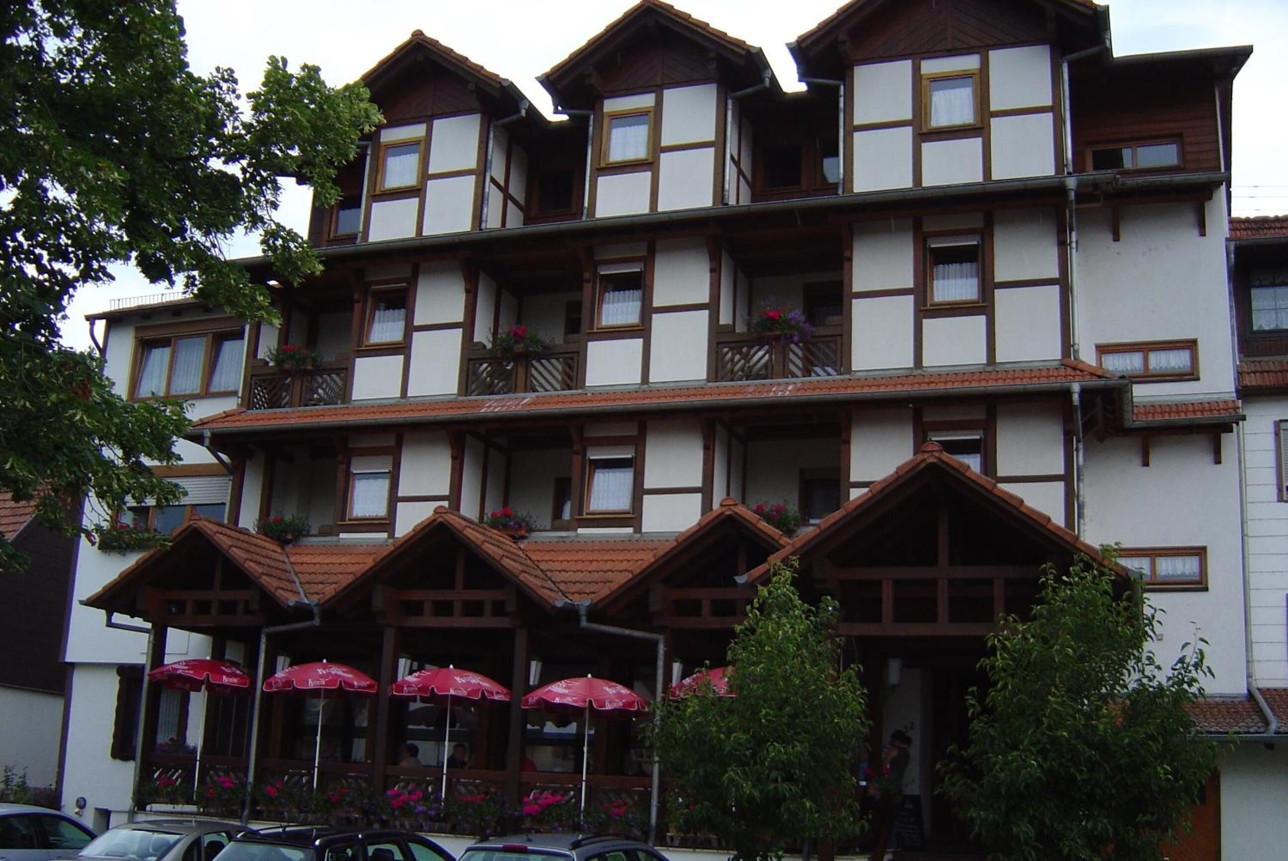 Un hotel de varios pisos con un estilo arquitectónico tradicional, que cuenta con balcones con jardineras y un área de estar exterior cubierta con sombrillas.
