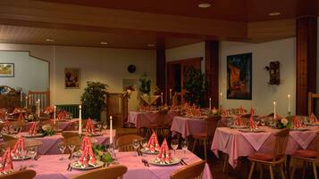 Un comedor con varias mesas dispuestas para una comida, con manteles rosas y centros de mesa florales rojos.