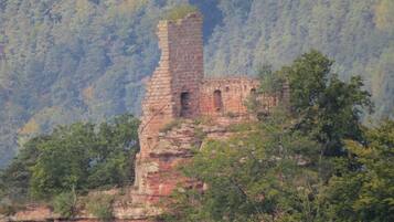 A historic stone structure perched on a cliff with dense forest in the background.
