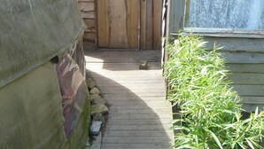 A wooden cabin with a door, a window with a curtain, and a wooden deck leading to the entrance. - Yurt Luxury & Bathouse (Callington)