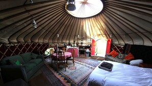 A yurt interior with a central table, chairs, a bed, and a rug. - Yurt Luxury & Bathouse (Callington)
