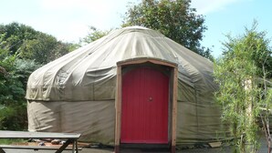 A round, covered structure with a red door, a wooden deck, and a picnic table. - Yurt Luxury & Bathouse (Callington)