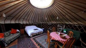 A yurt interior with a bed, sofa, dining table, and chairs. - Yurt Luxury & Bathouse (Callington)