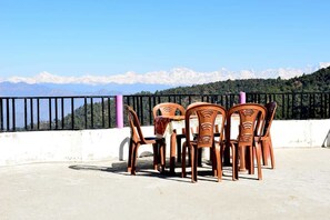 A terrace with a table and chairs, a view of mountains, and a railing. - Hotel Taj Himalaya khirsu (Srinagar)