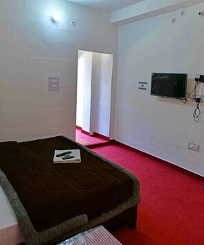 A room with a bed, a TV mounted on the wall, and a red carpet. - Hotel Taj Himalaya khirsu (Srinagar)