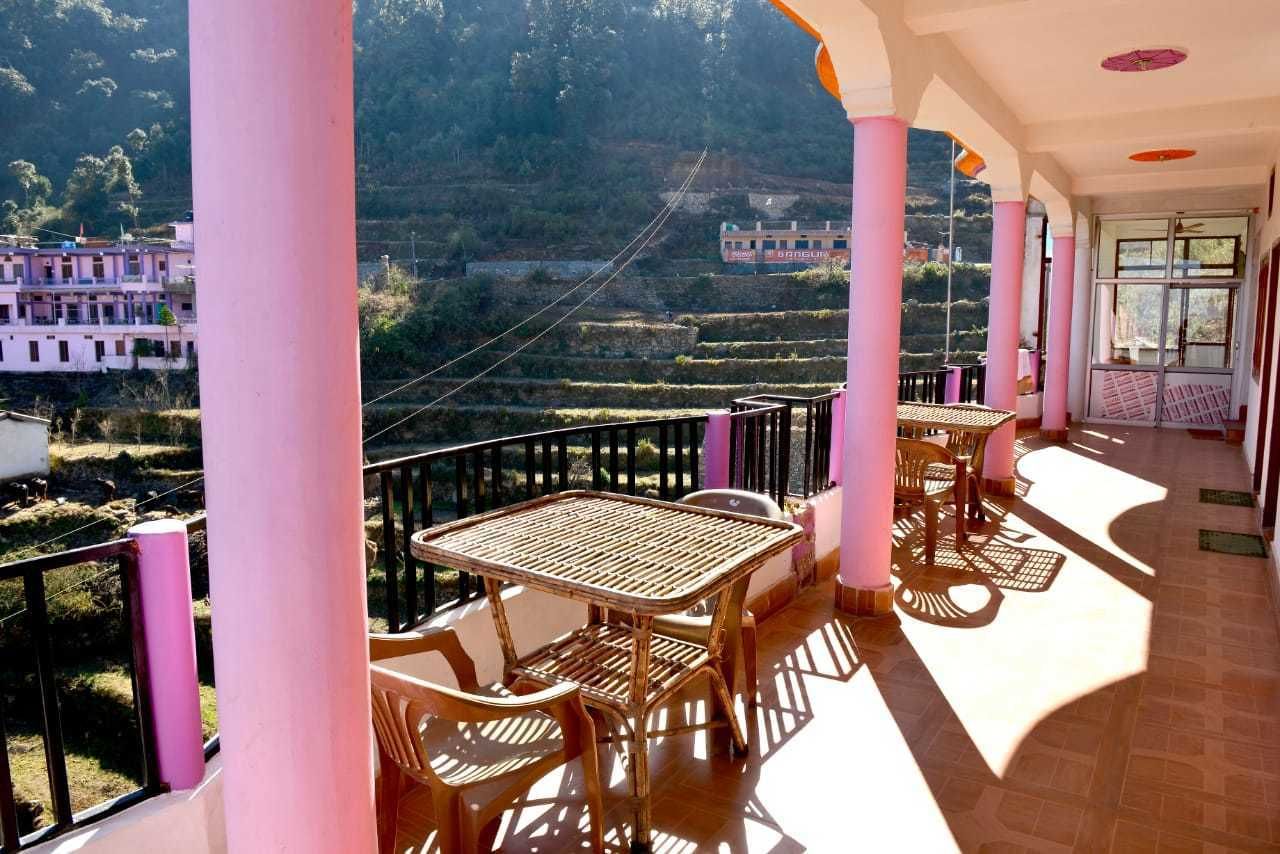 A balcony with a table and chairs, overlooking terraced fields and buildings.