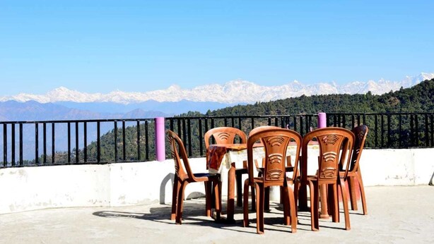 A terrace with four wooden chairs and a table, overlooking a mountainous landscape with snow-capped peaks. - Hotel Taj Himalaya khirsu (Srinagar)
