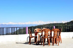 A terrace with four wooden chairs and a table, overlooking a mountainous landscape with snow-capped peaks.