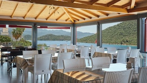 A covered outdoor seating area with wicker chairs and tables, overlooking a body of water and hills. - Kaskoy Hotel (Kas)