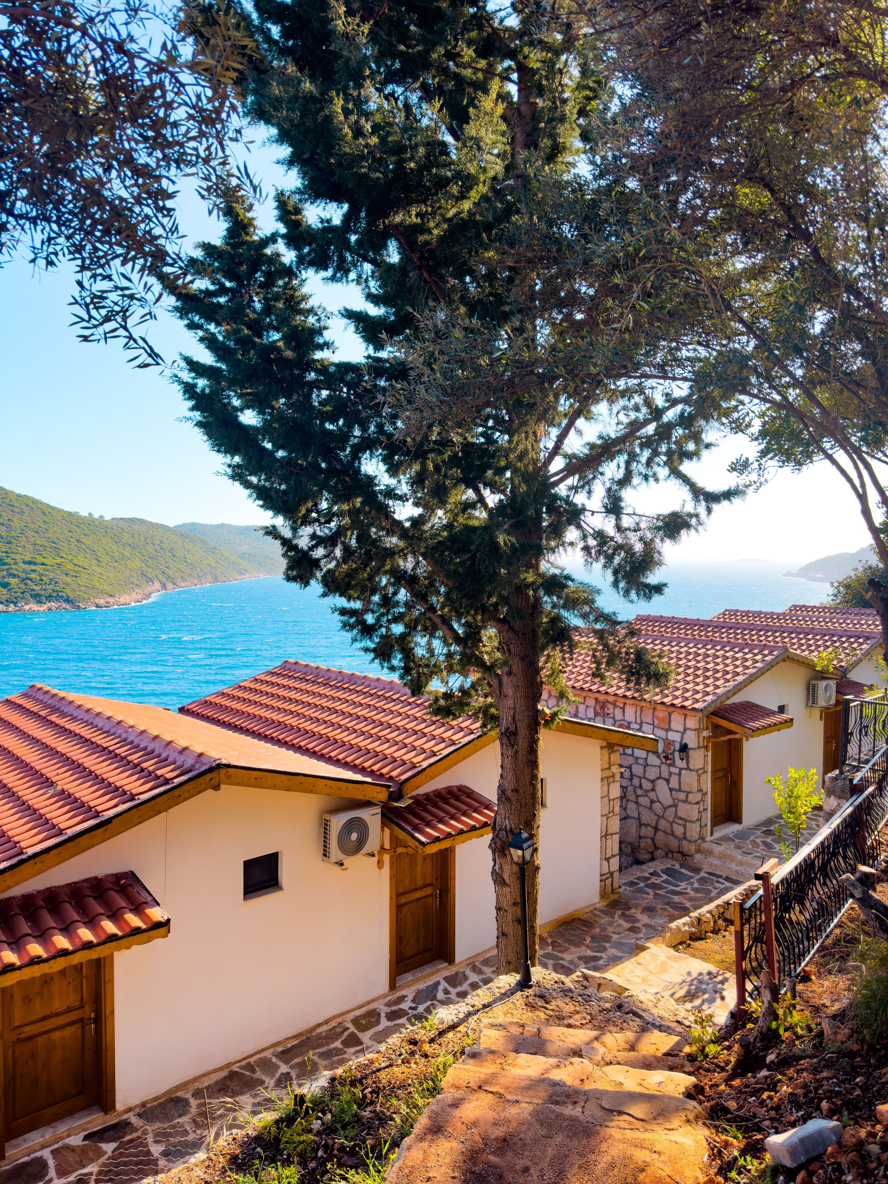 A coastal building with red-tiled roofs, stone walls, and a view of the sea.