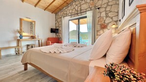 A bedroom with a stone wall, wooden ceiling, a bed with white linens, a wooden nightstand, a TV, and a view of the outside. - Kaskoy Hotel (Kas)