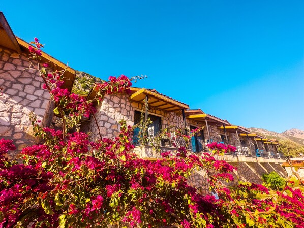 Un edificio de piedra con un balcón de madera y flores de buganvilla rosadas.