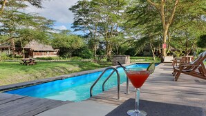A poolside area with a wooden deck, lounge chairs, and a drink on a table. - Swara Acacia Lodge (Athi River)