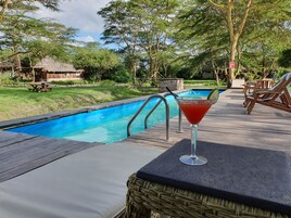 A poolside area with a wooden deck, lounge chairs, and a drink on a table.
