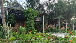 A rustic garden with traditional wooden structures, lush greenery, and a variety of flowering plants. - Swara Acacia Lodge (Athi River)