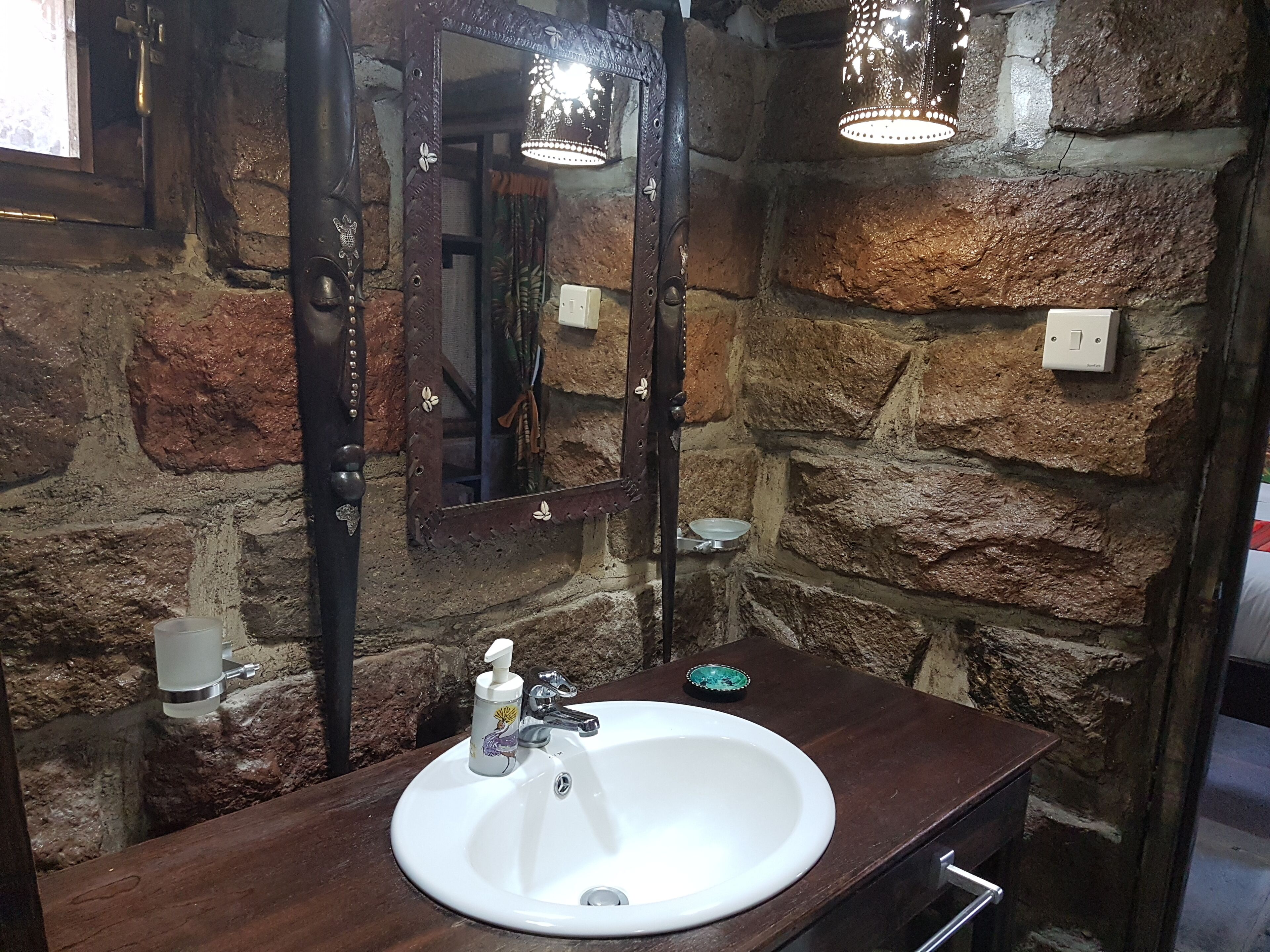 A bathroom with a white sink, a mirror, and a stone wall.