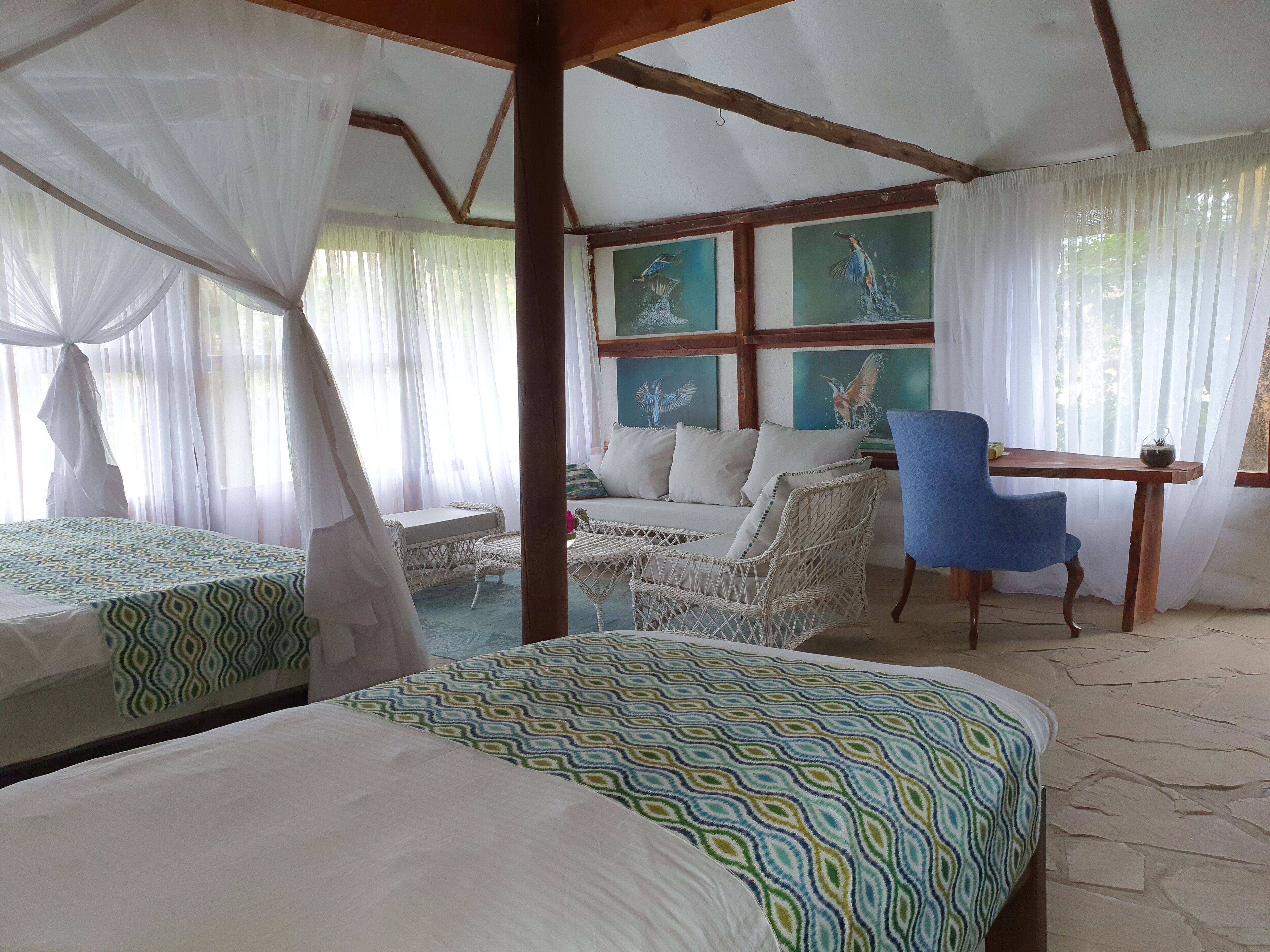 Una habitación con una cama, un sofá, una silla y una mesa. Hay cuadros en la pared y una ventana con cortinas.