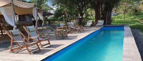 Una piscina con sillones de madera y una zona de estar cubierta.