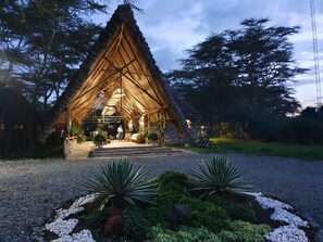 A thatched-roof structure with a central seating area, surrounded by potted plants and a gravel path. - Swara Acacia Lodge (Athi River)