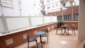 A terrace with a table and chairs, a potted plant, and a view of adjacent buildings. - Amazing Napoli (Naples)