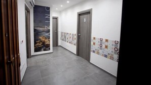 A hallway with grey tiled flooring, a wall with a colorful patchwork design, and a door with a triangular symbol. - Amazing Napoli (Naples)