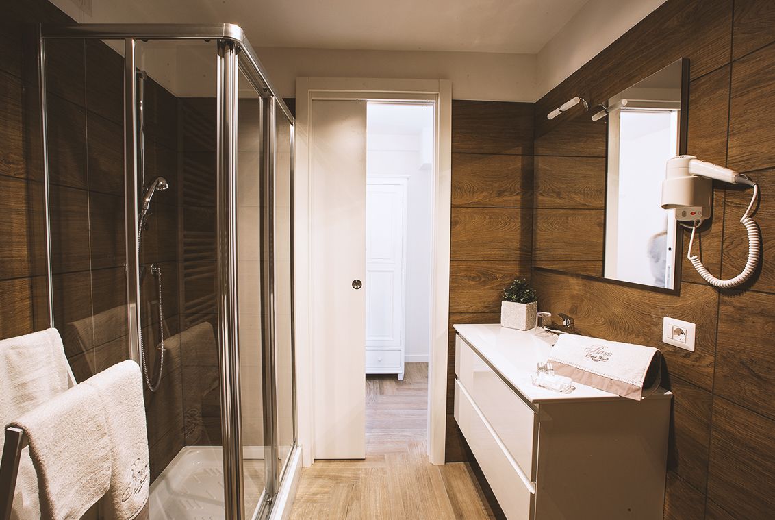 A modern bathroom with a glass-enclosed shower, a vanity with a mirror, and a hairdryer mounted on the wall.