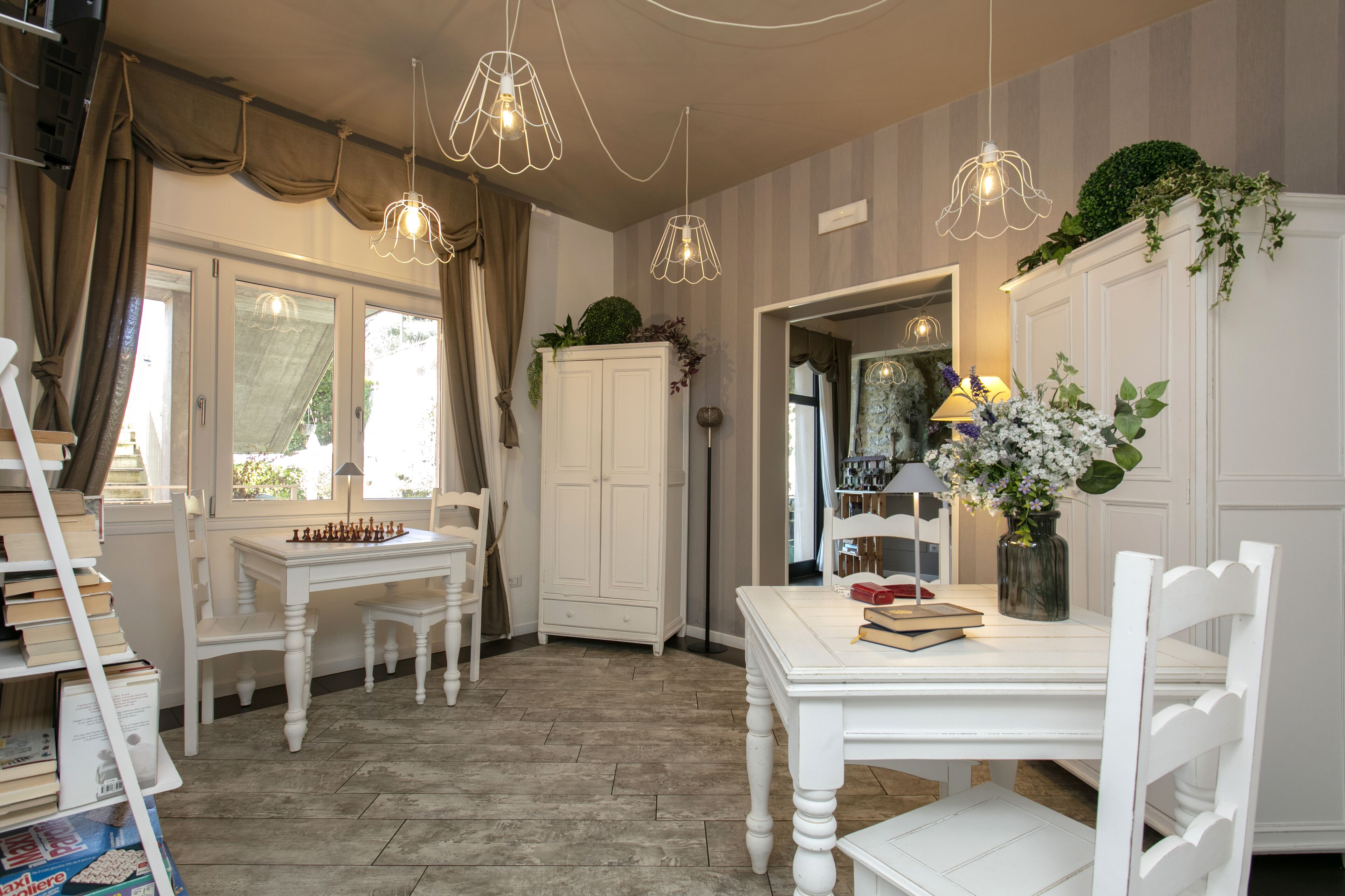 A room with a white table, chairs, a chessboard, a bookshelf, and a cabinet with greenery.