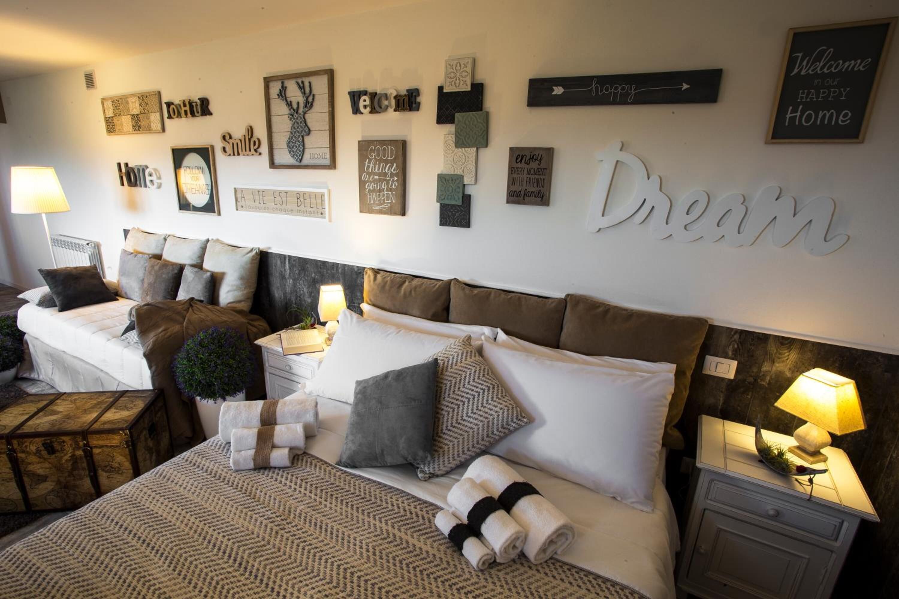 Habitación de hotel con dos camas, un reloj de pared grande y varias obras de arte con mensajes motivacionales.