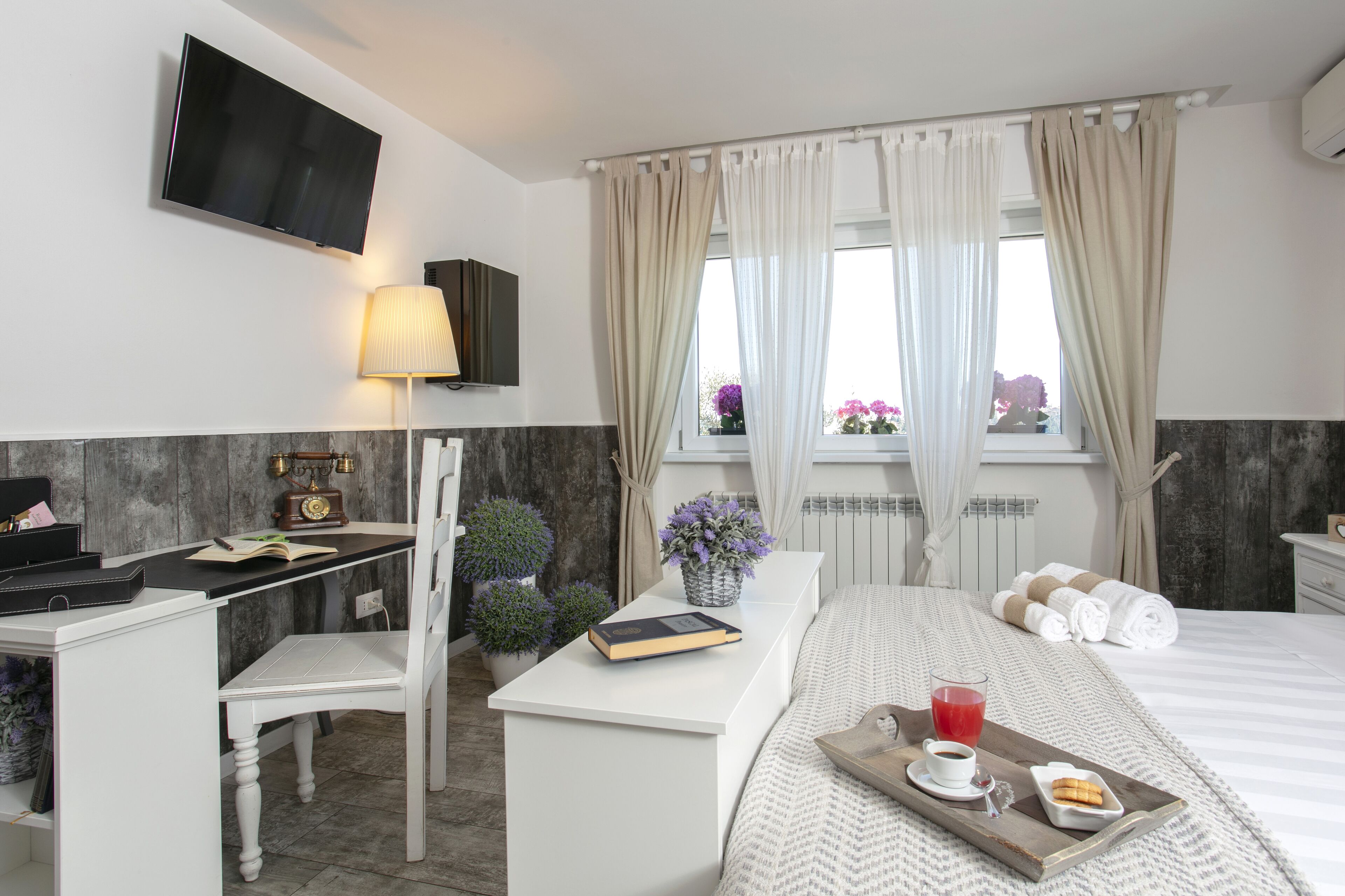 A hotel room with a bed, a desk with a lamp, a TV, and a window with curtains.