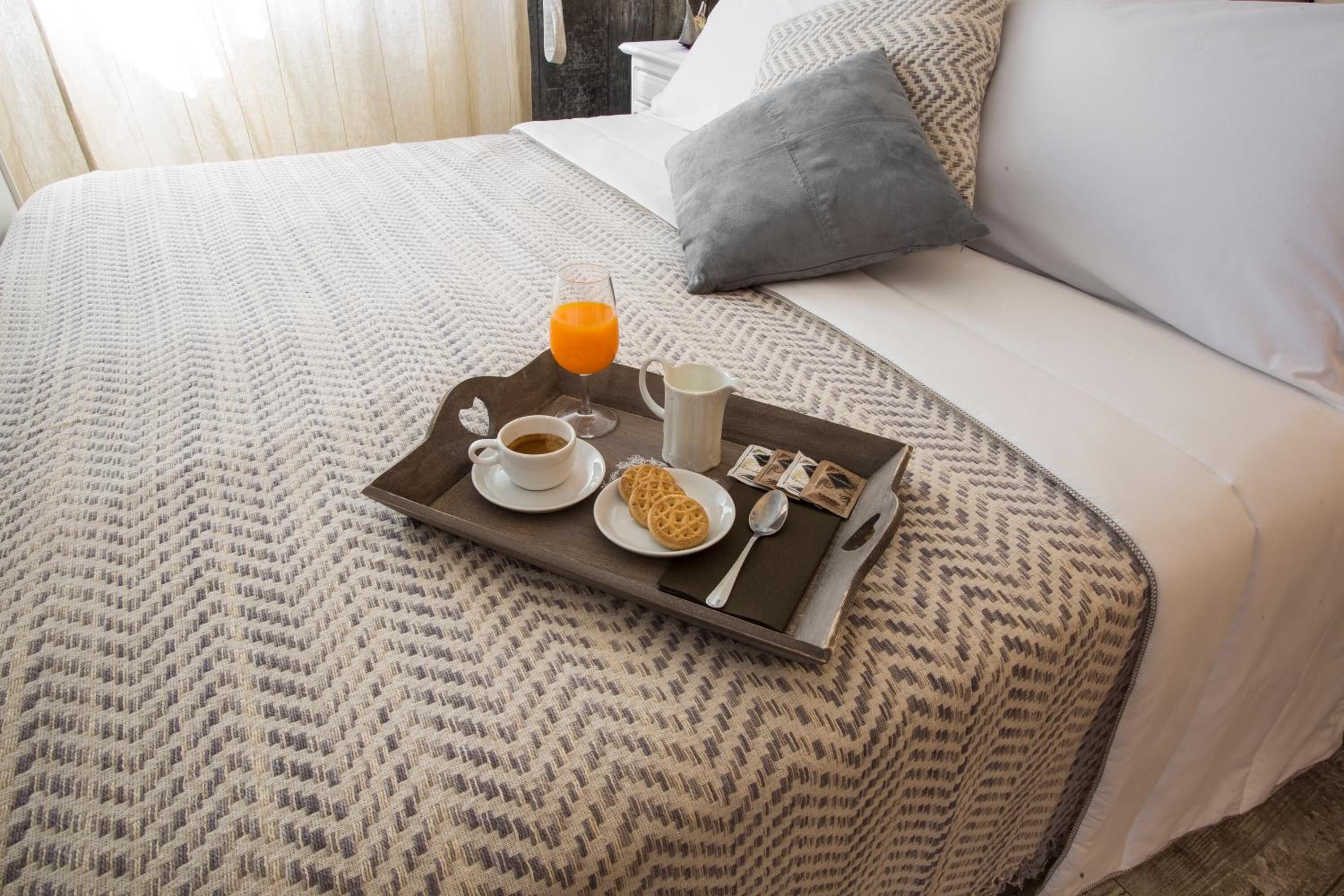 A neatly made bed with a tray of breakfast items including a glass of orange juice, a cup of coffee, a plate with biscuits, and a small pitcher.