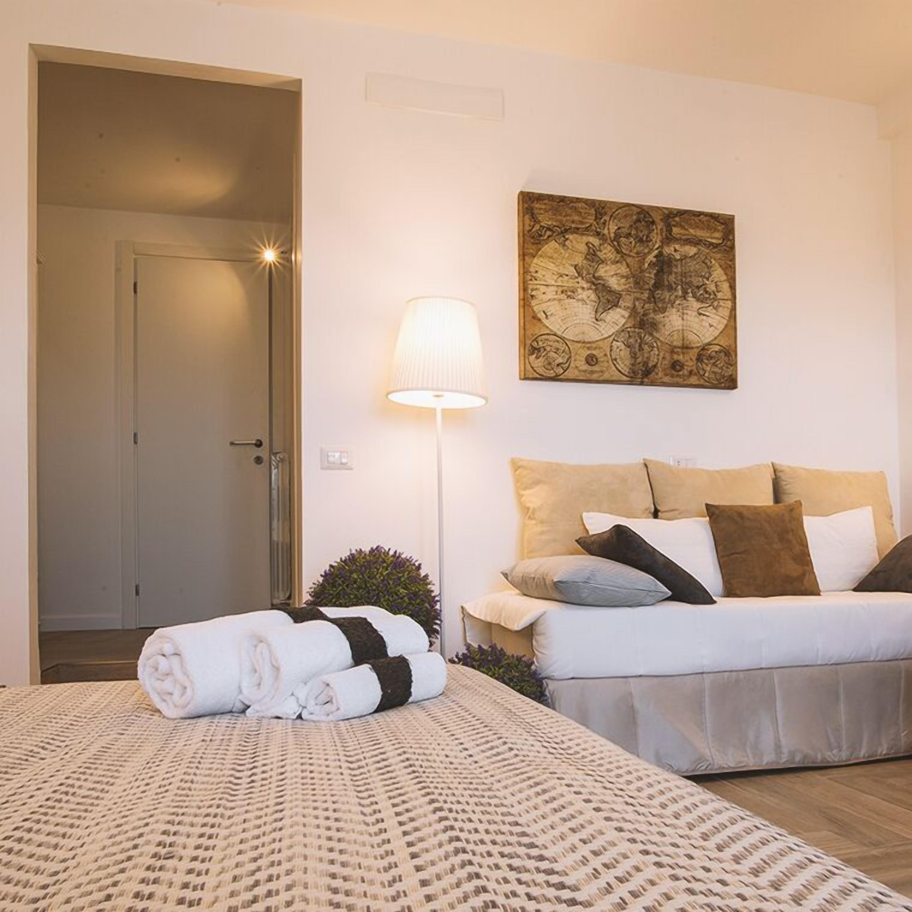 A hotel room with a bed, a bedside lamp, a map on the wall, and a door leading to another room.