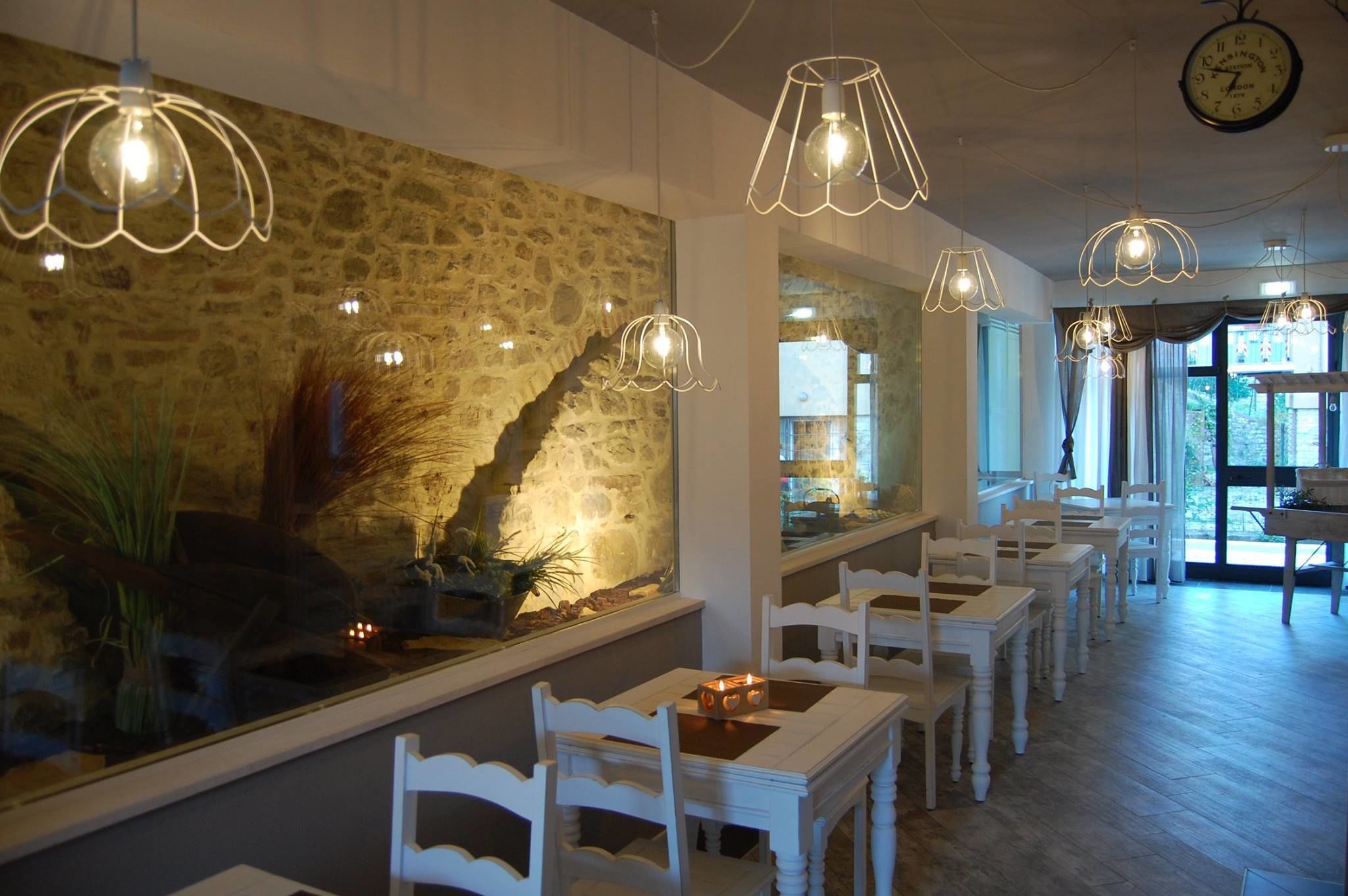 A restaurant with stone walls, white chairs, and hanging pendant lights.