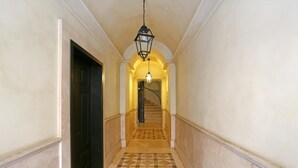 Un couloir doté d’un sol carrelé, une porte noire sur la gauche et un escalier sur lequel est fixée une lampe.