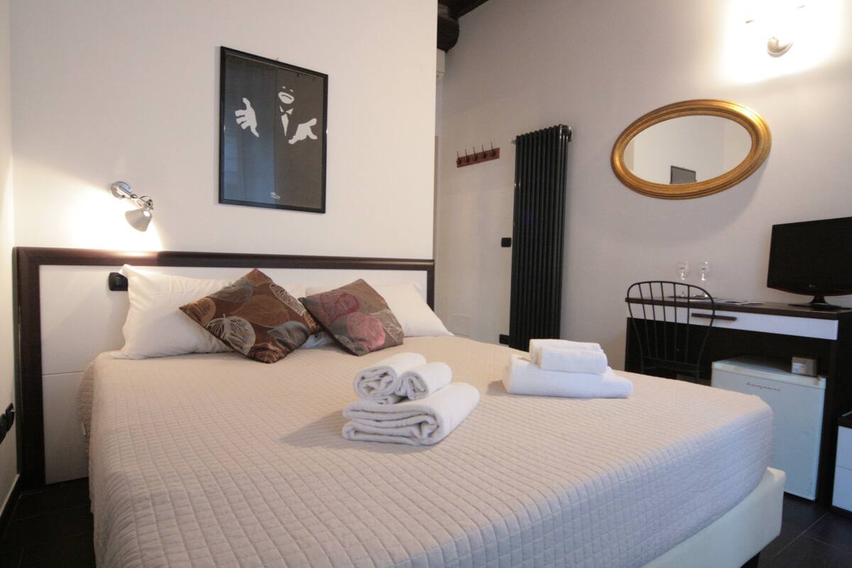 A neatly made bed with pillows, a folded towel, and a bedside table with a lamp.