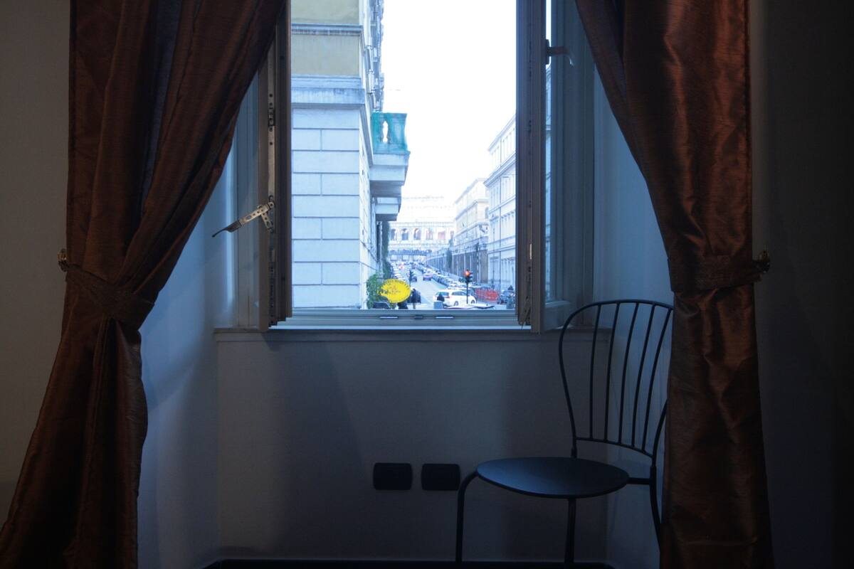 A room with a window, curtains, a chair, and a wall switch.
