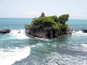 Une île rocheuse abritant un temple balinais traditionnel et une végétation luxuriante, le tout entouré d’une mer turquoise.