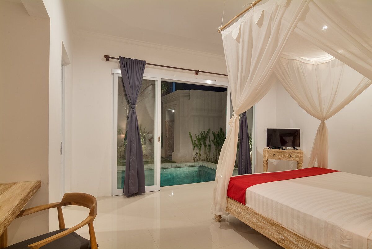 Une chambre à coucher avec un lit à baldaquin, un téléviseur posé sur une table de chevet en bois, et une vue sur une piscine à travers des portes vitrées.
