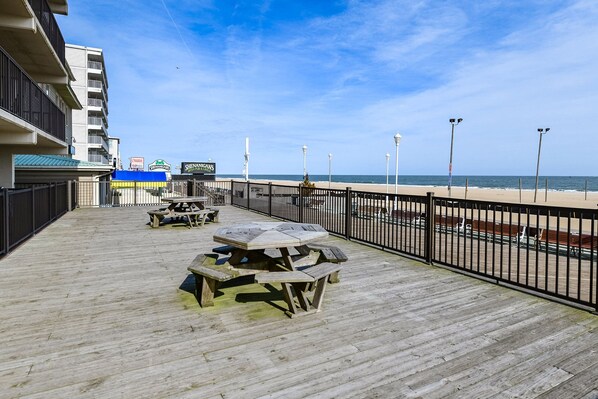 A wooden deck with picnic tables, a beach view, and a building with a sign for a pub and grill.