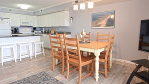 A modern kitchen with white cabinets, a wooden dining table, and a large island with bar stools.