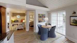 Een ruime woonkamer met een hoge plafond, een eetgedeelte met een ronde tafel en stoelen, en uitzicht door grote ramen.