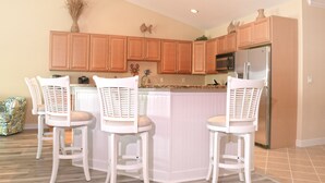 A kitchen with wooden cabinets, a stainless steel refrigerator, and a white island with bar stools. - Stylish, upscale luxury 4-bedroom condo with free WiFi and an outdoor pool located downtown on the bay water and just a few blocks to the beach! (Ocean City)