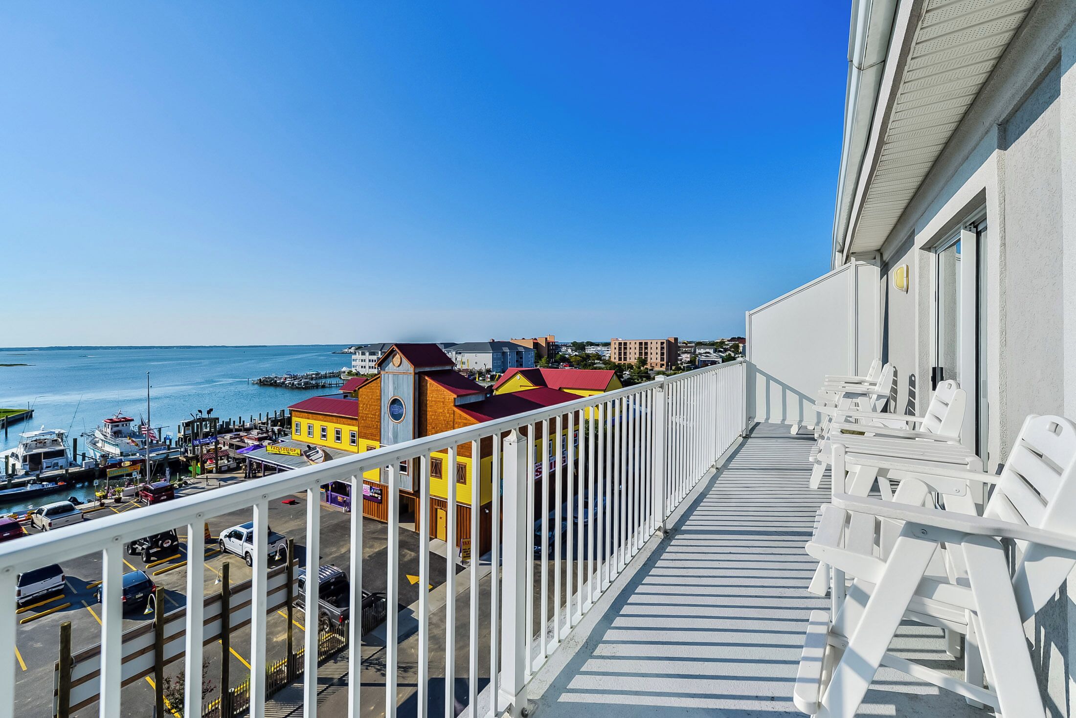 A balcony with white chairs overlooking a marina with boats and colorful buildings.