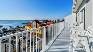 A balcony with white chairs overlooking a marina with boats and colorful buildings. - Stylish, upscale luxury 4-bedroom condo with free WiFi and an outdoor pool located downtown on the bay water and just a few blocks to the beach! (Ocean City)