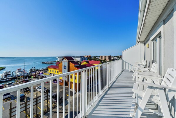A balcony with white chairs overlooking a marina with boats and colorful buildings. - Stylish, upscale luxury 4-bedroom condo with free WiFi and an outdoor pool located downtown on the bay water and just a few blocks to the beach! (Ocean City)