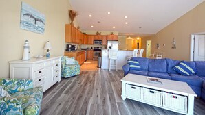 A spacious living area with a sofa, a coffee table, and a dining area with wooden cabinets and a refrigerator. - Stylish, upscale luxury 4-bedroom condo with free WiFi and an outdoor pool located downtown on the bay water and just a few blocks to the beach! (Ocean City)