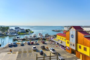 A marina with boats docked, a parking lot with cars, and buildings with a red roof and a yellow facade. - Stylish, upscale luxury 4-bedroom condo with free WiFi and an outdoor pool located downtown on the bay water and just a few blocks to the beach! (Ocean City)