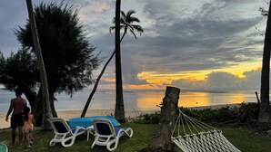 Une scène de plage avec deux chaises longues et un hamac, une petite tente et le tronc d’un arbre.